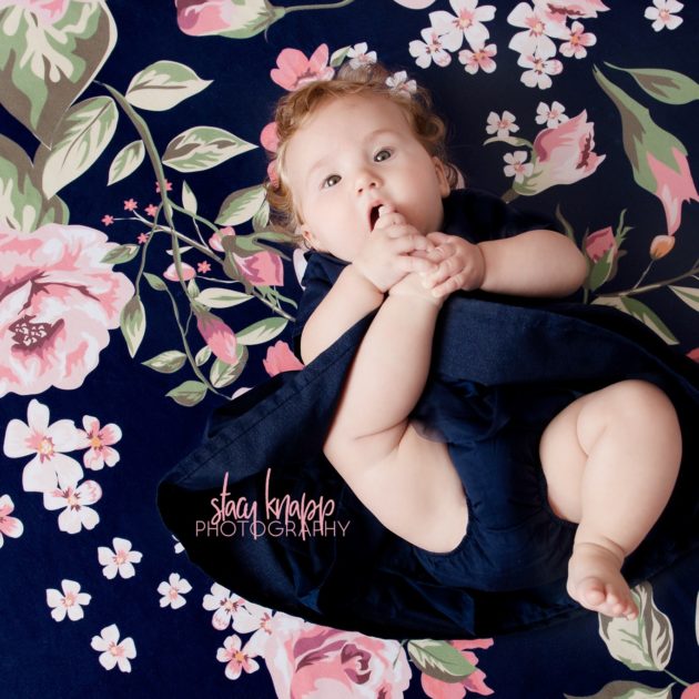 Baby girl photographed in navy blue dress with pearls on a navy blue floral backdrop