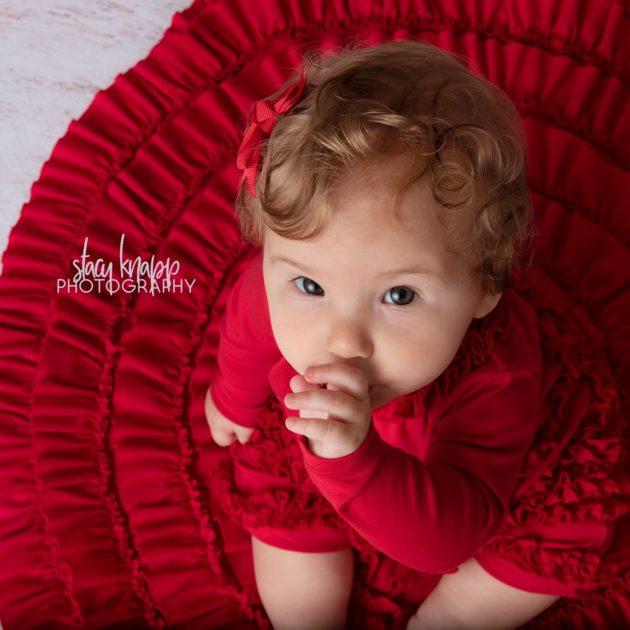 Baby girl photographed wearing red on a red stocking holiday backdrop