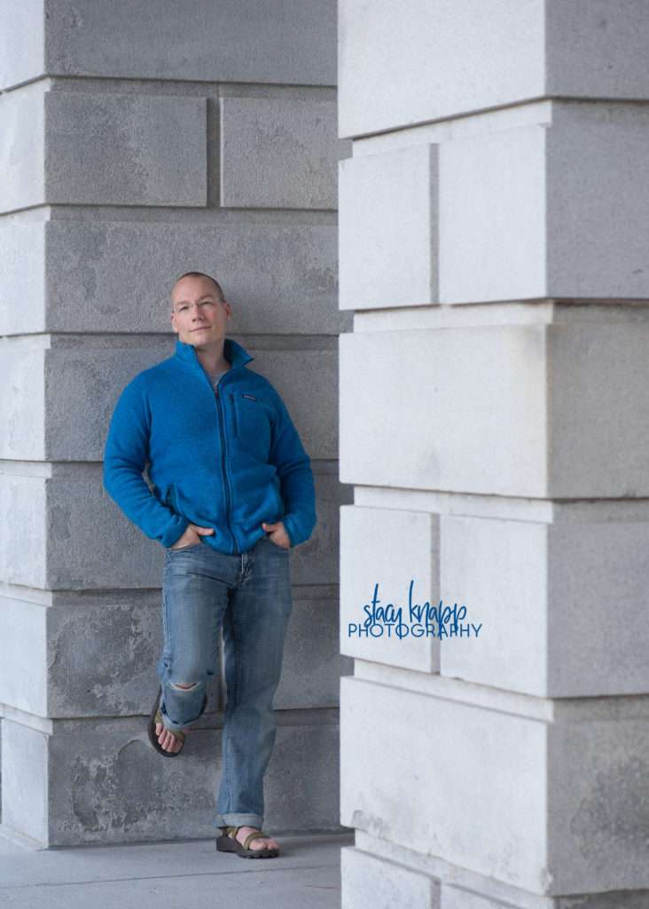 Headshot of photograph a man standing in front of the State House in Augusta Maine wearing blue
