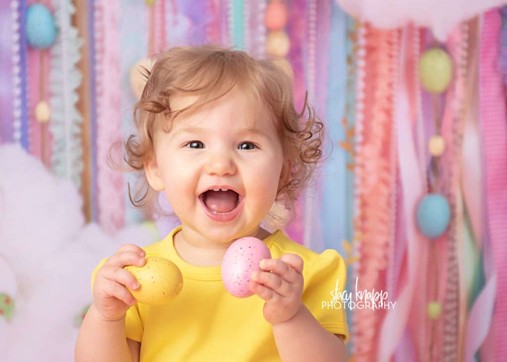 Baby girl Easter photograph on an Easter egg backdrop during a mini session