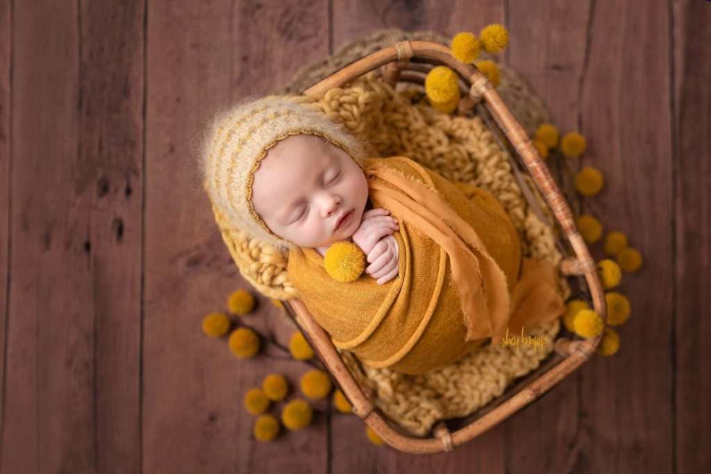 Newborn baby girl baby wrapped in yellow in bamboo box with yellow bonnet