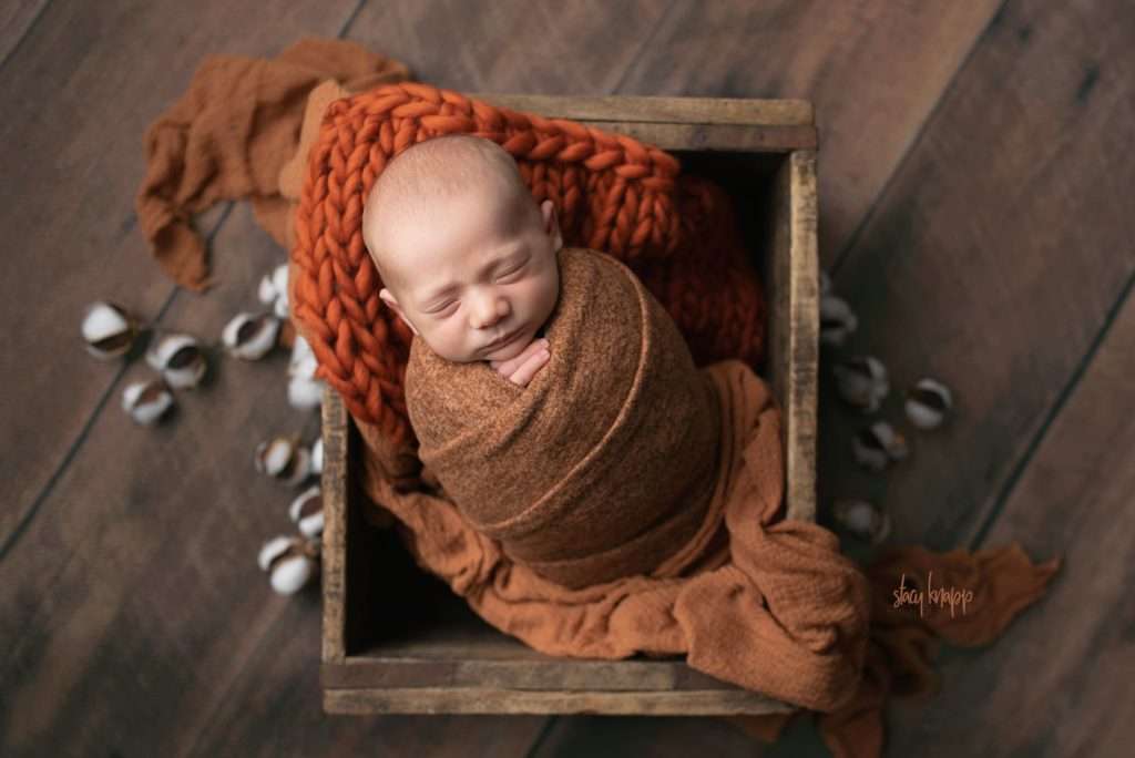 Newborn baby boy in rust wrap in crate