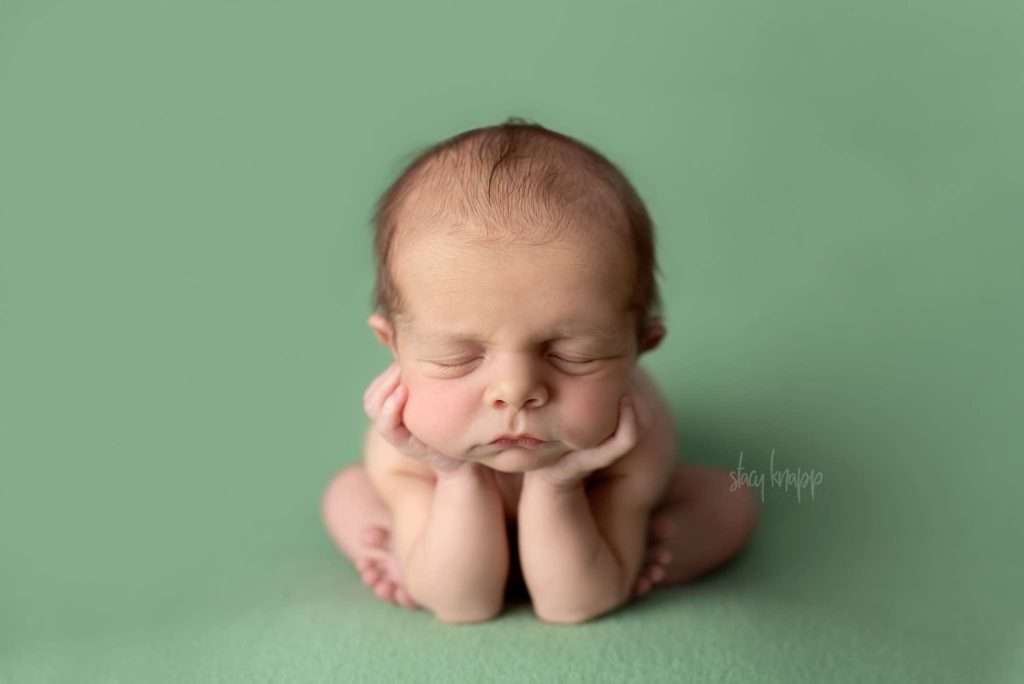 Newborn baby boy in froggy pose on green