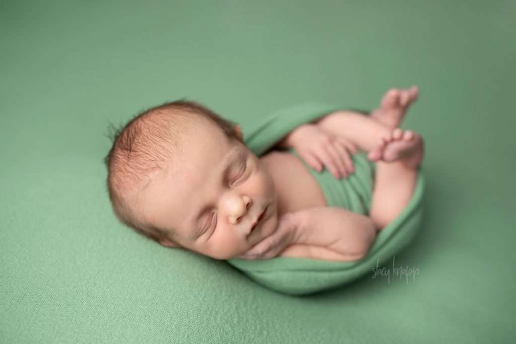 Newborn baby boy in egg wrap on green