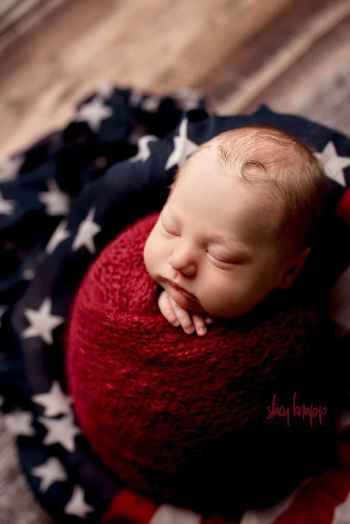 Newborn baby boy in red knit wrap with American Flag
