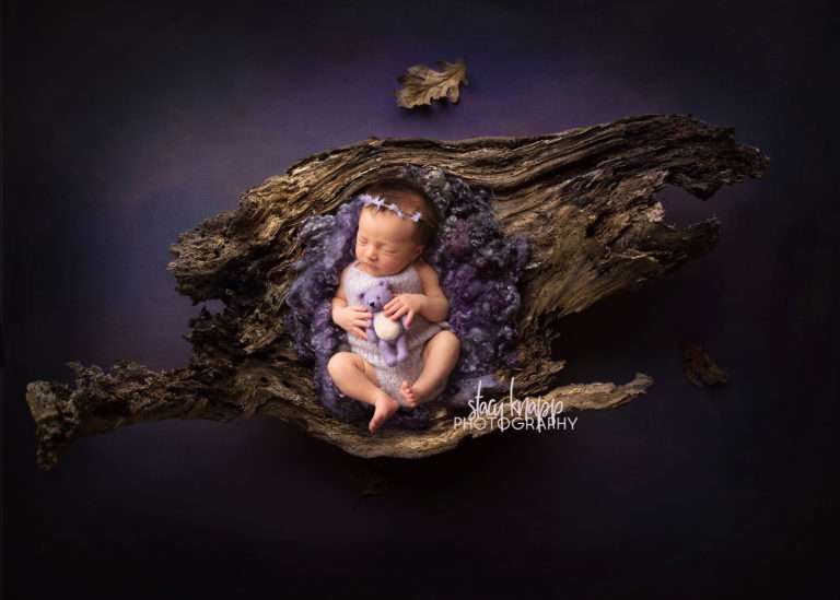 newborn baby girl photo of baby in purple curls on wood bark