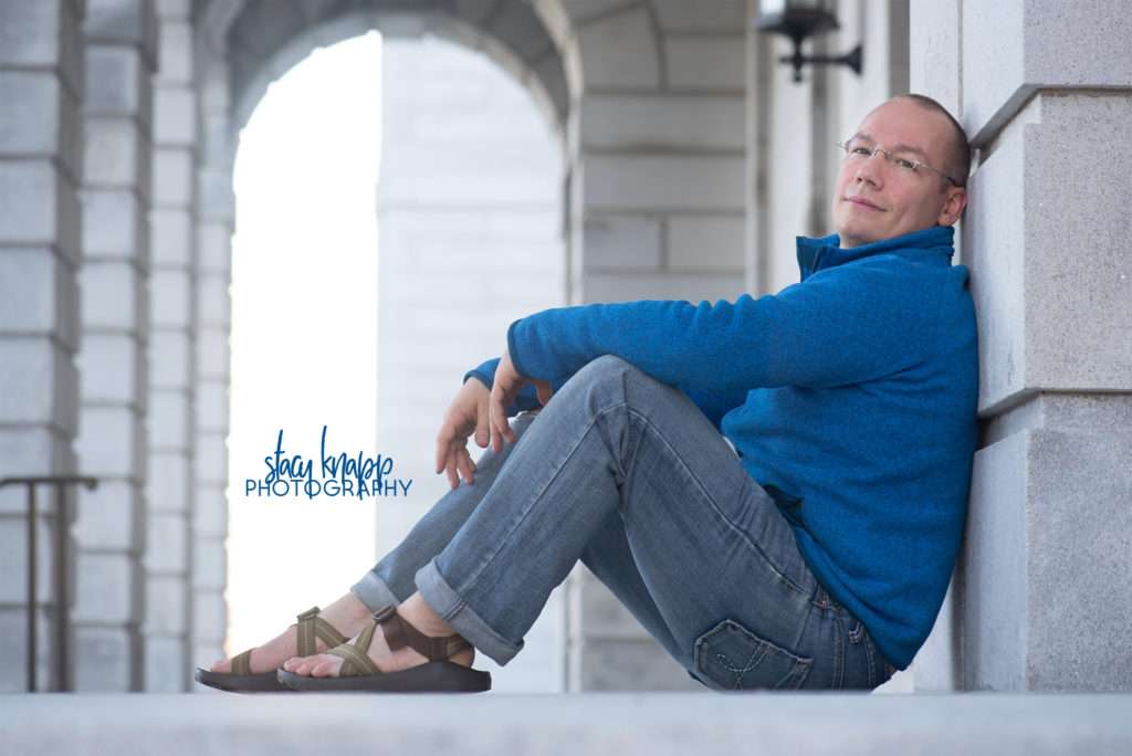 Headshot of photograph a man sitting on steps of the State House in Augusta Maine wearing blue