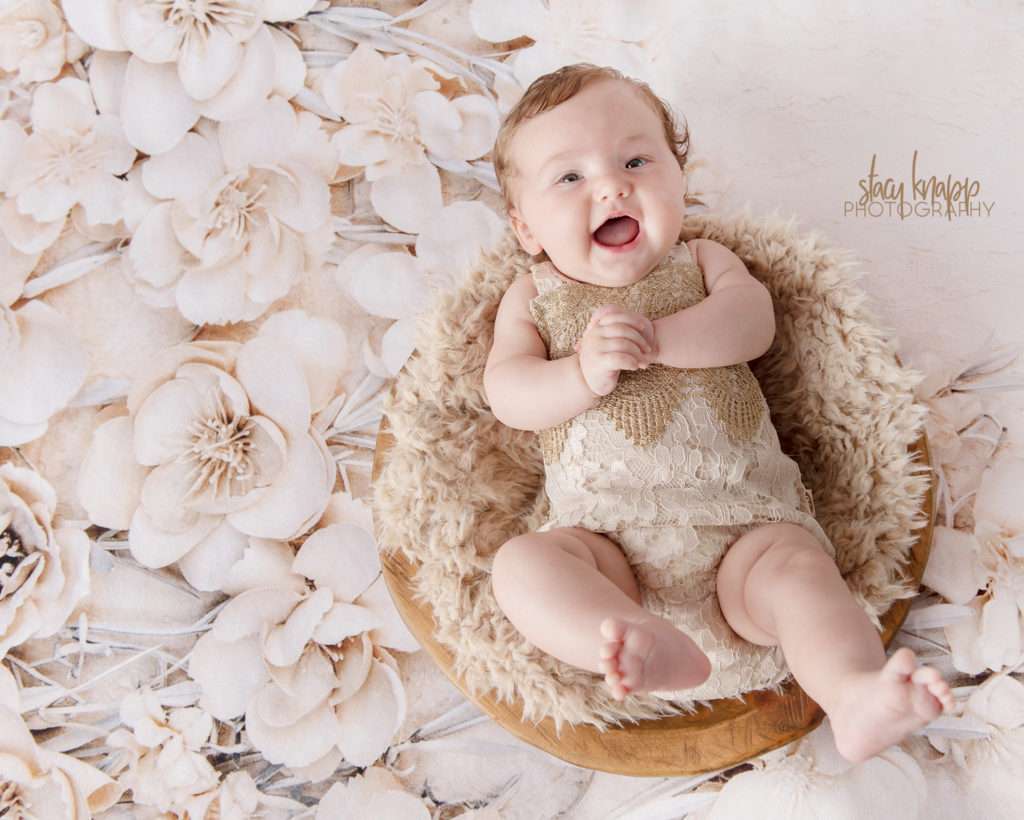Baby girl photographed wearing beige outfit with floral backdrop