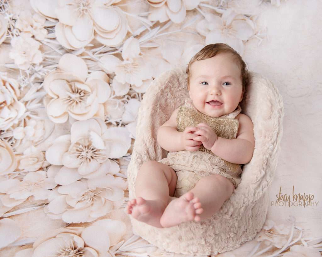 Baby girl photographed wearing beige outfit with floral backdrop