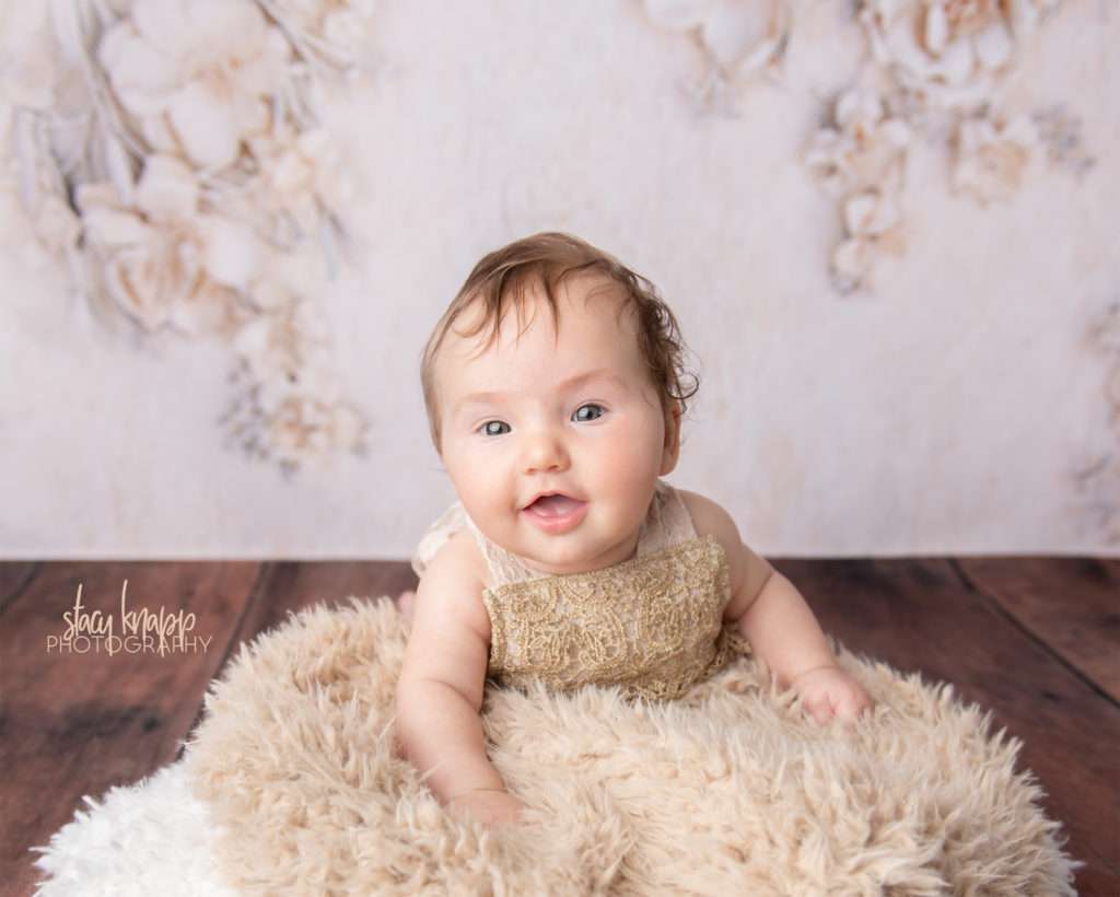 Baby girl photographed wearing beige outfit with floral backdrop