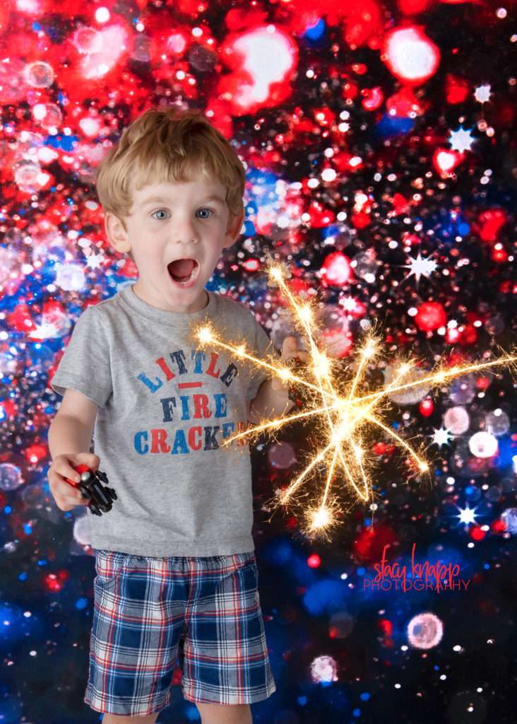 Toddler boy photographed on Forth of July backdrop with sparkler