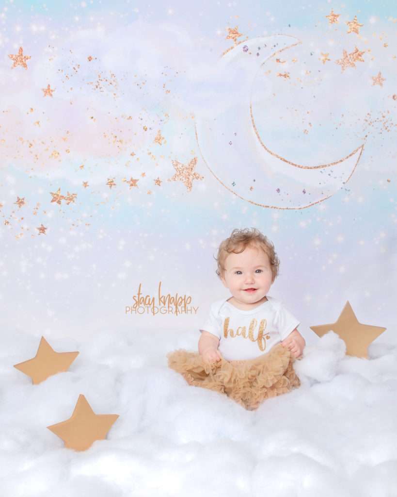 Six-month-old (half year) baby girl photographed in cloud scene with gold tutu