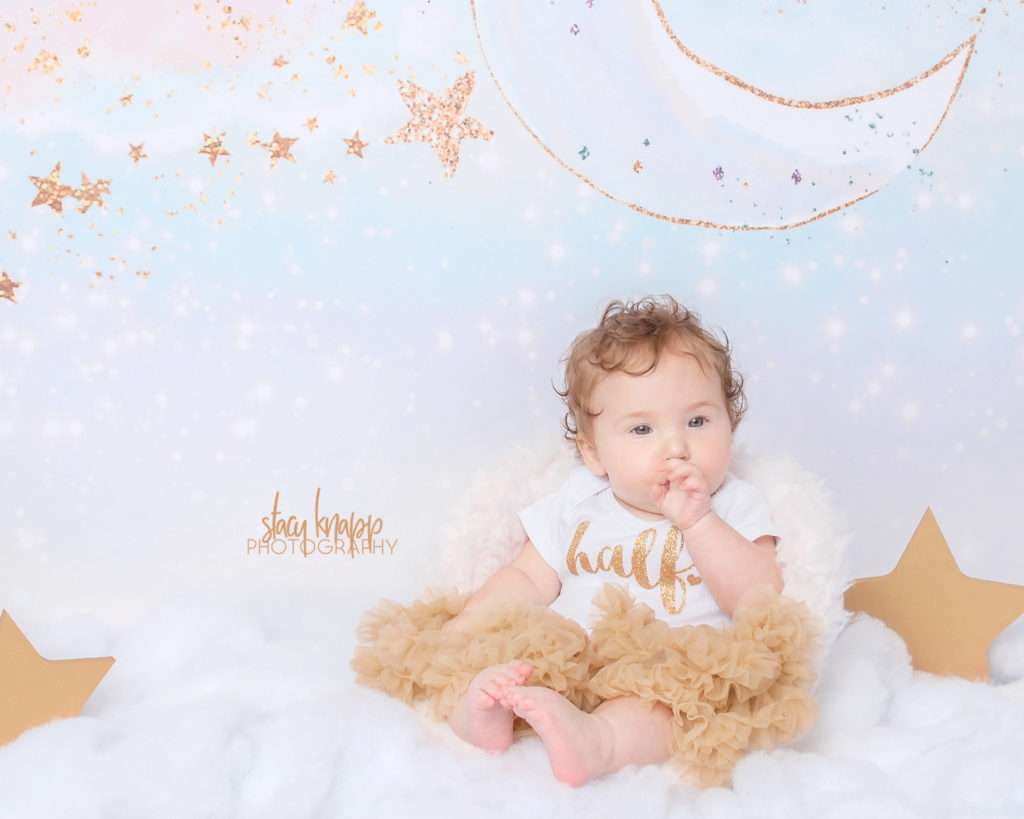 Six-month-old (half year) baby girl photographed in cloud scene with gold tutu