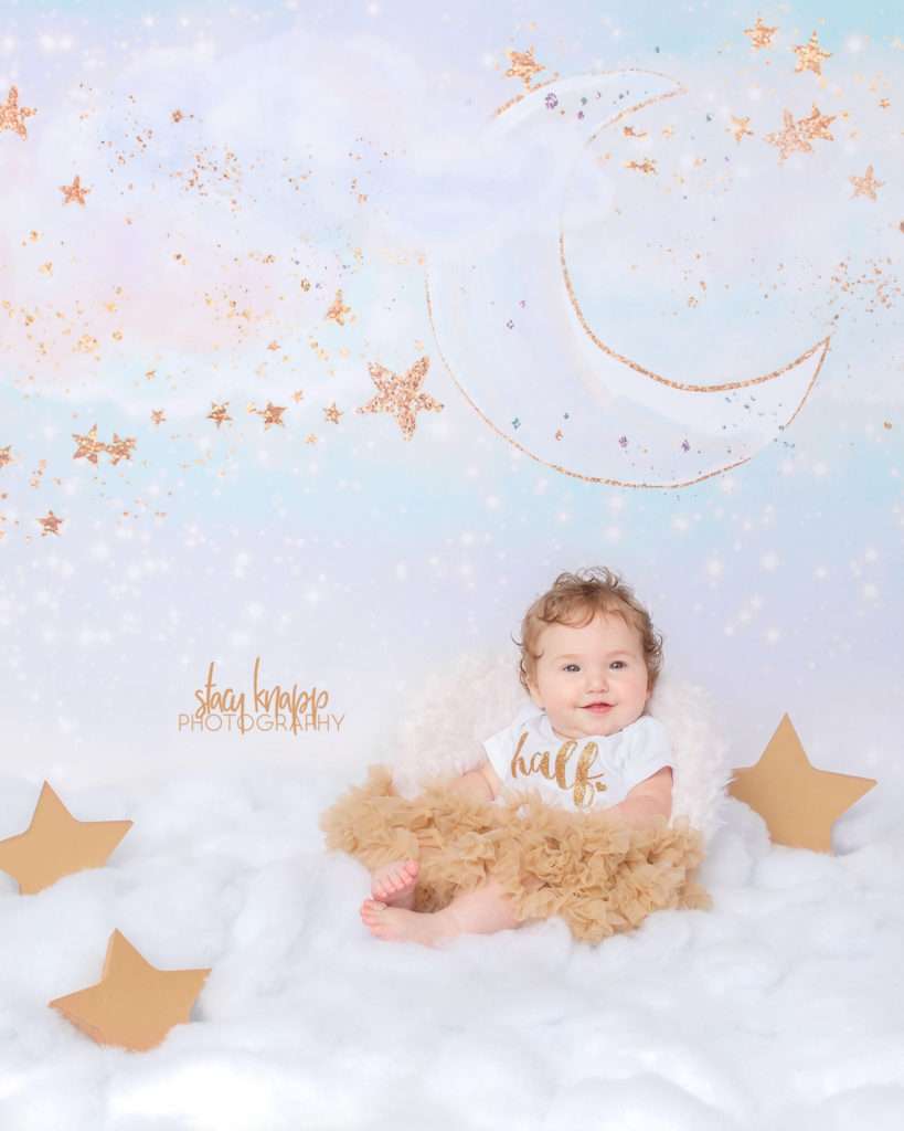 Six-month-old (half year) baby girl photographed in cloud scene with gold tutu