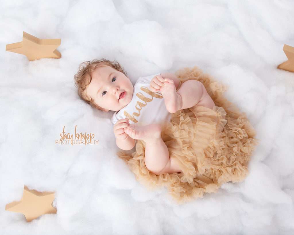 Six-month-old (half year) baby girl photographed in cloud scene with gold tutu
