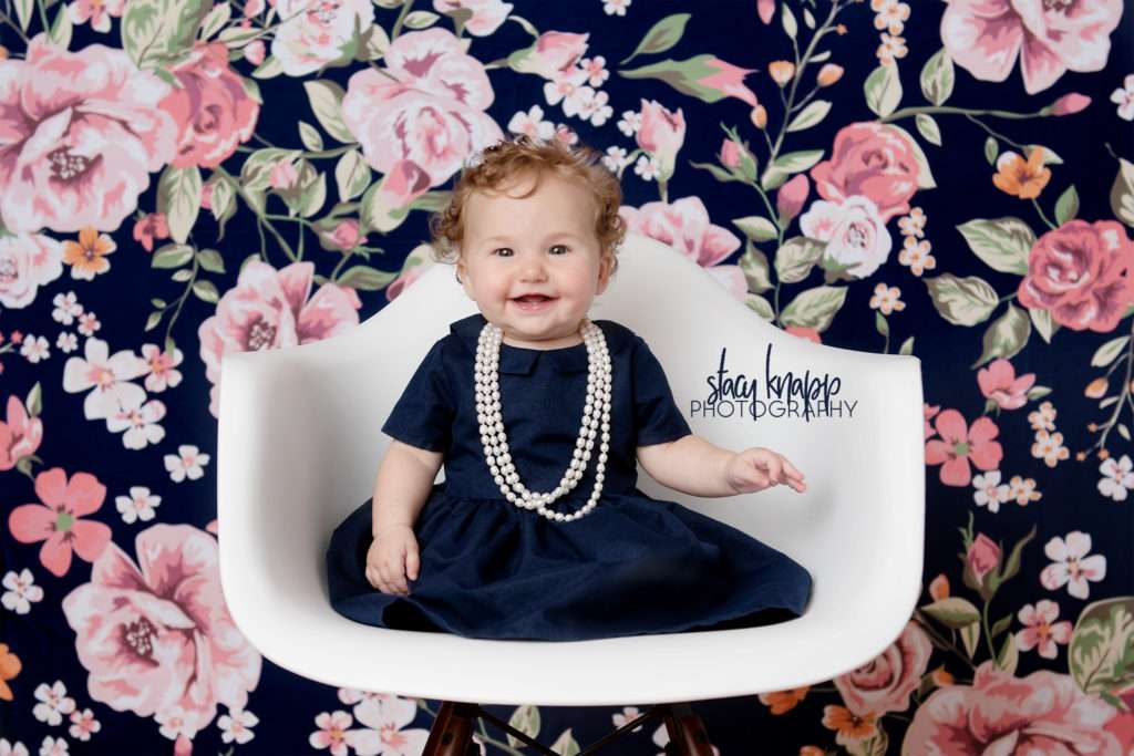 Baby girl photographed in navy blue dress with pearls on a navy blue floral backdrop