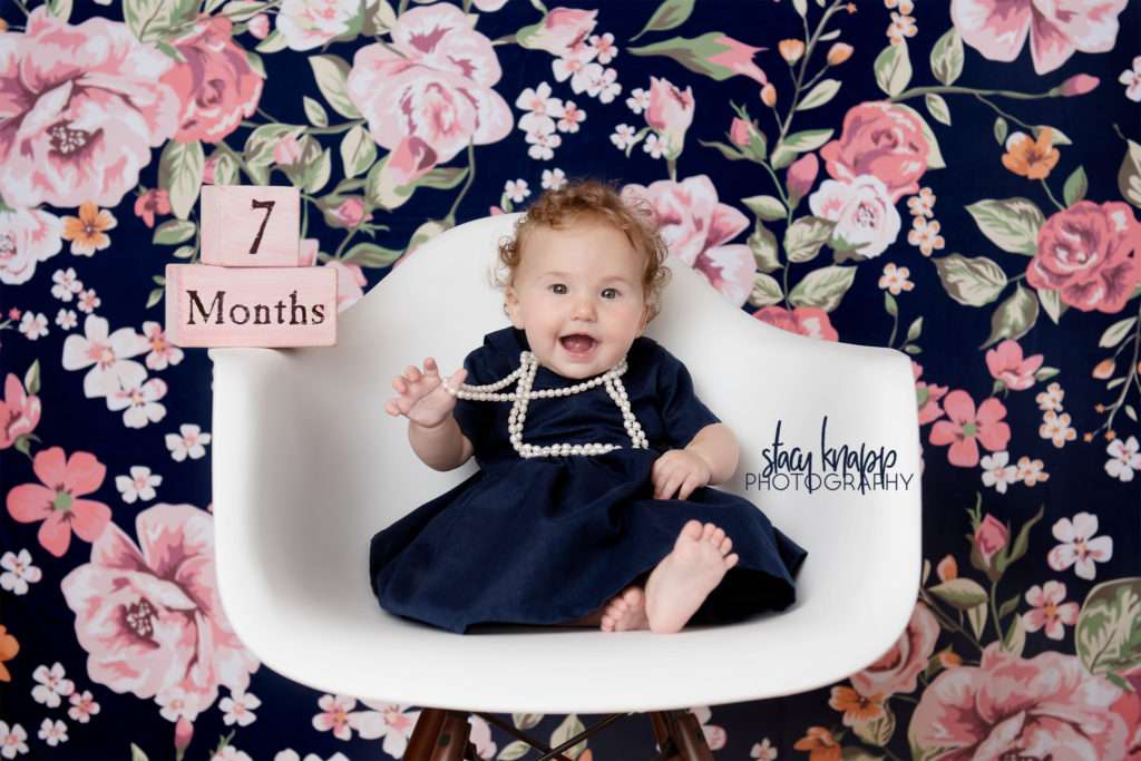 Baby girl photographed in navy blue dress with pearls on a navy blue floral backdrop