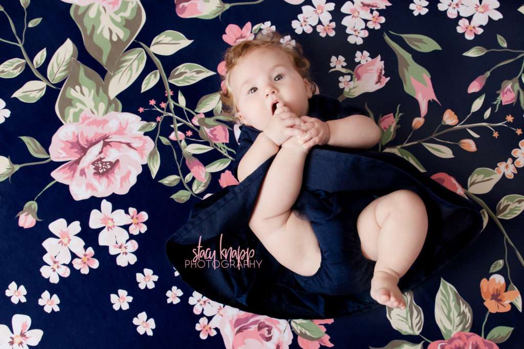Baby girl photographed in navy blue dress with pearls on a navy blue floral backdrop