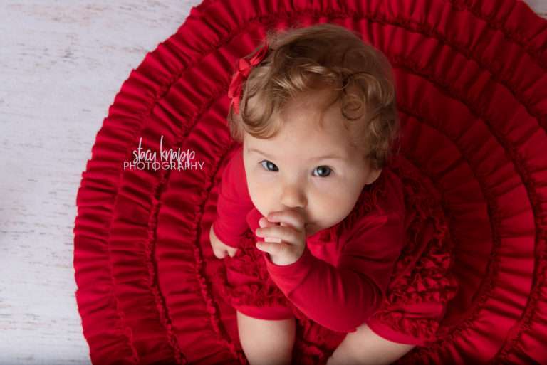 Baby girl photographed wearing red on a red stocking holiday backdrop