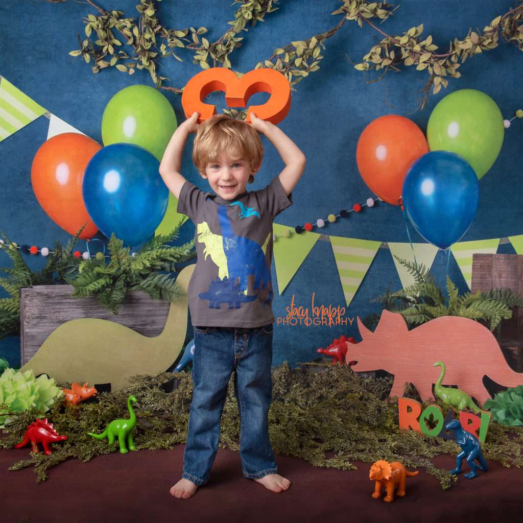Preschool boy age three photographed on dinosaur backdrop
