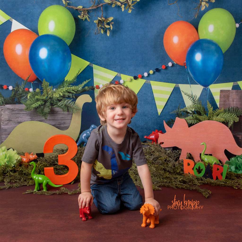Preschool boy age three photographed on dinosaur backdrop