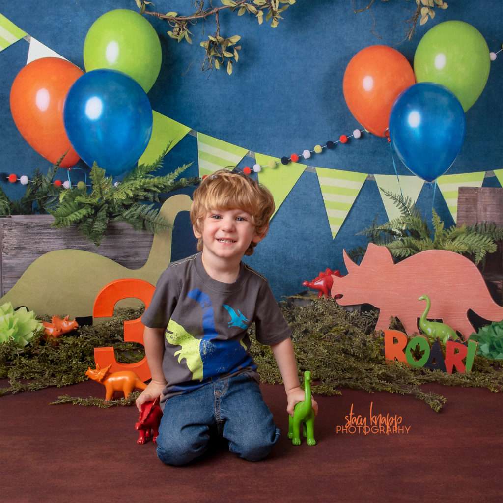 Preschool boy age three photographed on dinosaur backdrop