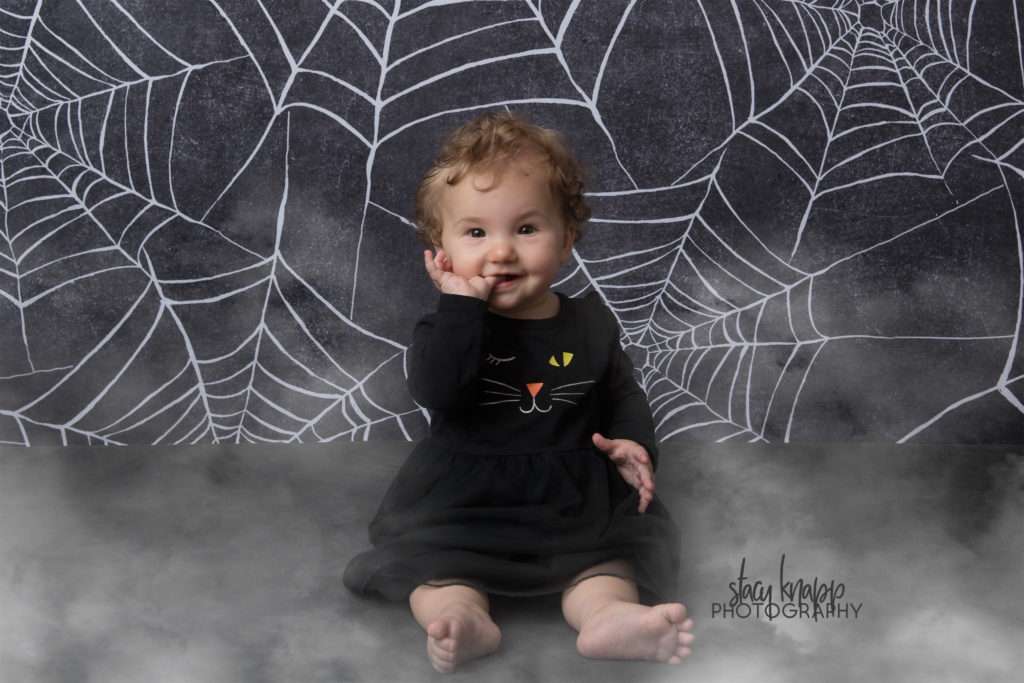 Baby girl photographed on Halloween backdrop wearing kitty outfit