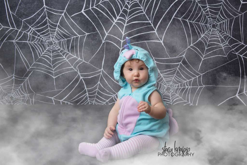 Baby girl photographed on Halloween backdrop wearing peacock costume