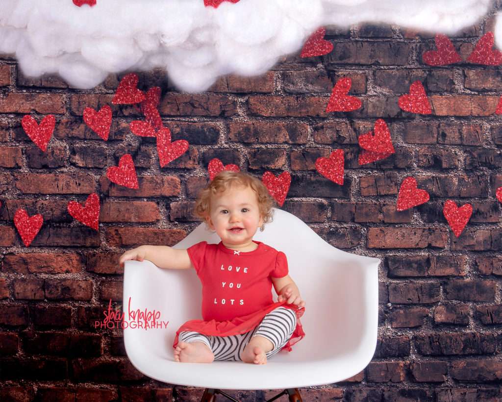 Baby girl photographed on Valentines Day backdrop with hearts and clouds during mini session