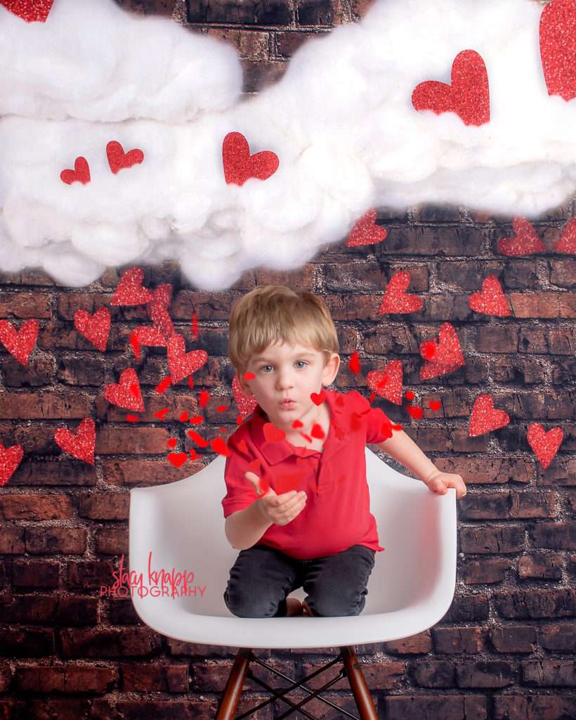 Preschool  boy photographed on Valentines Day backdrop with hearts and clouds during mini session