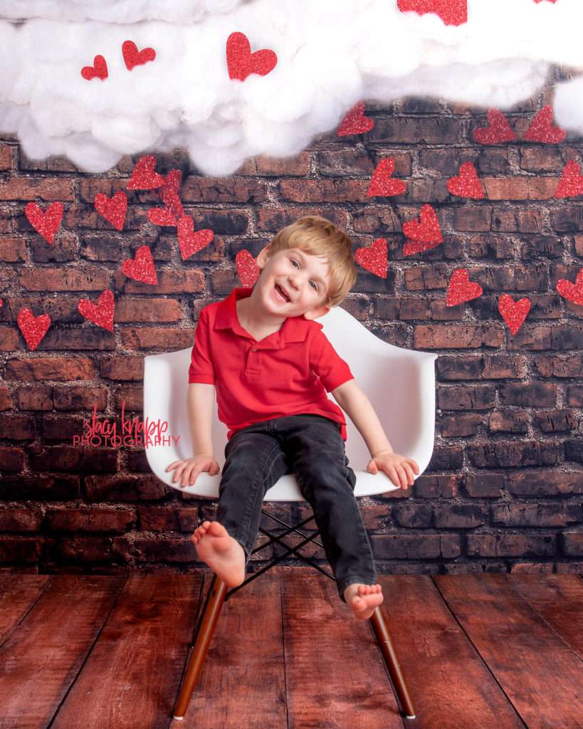 Preschool  boy photographed on Valentines Day backdrop with hearts and clouds during mini session
