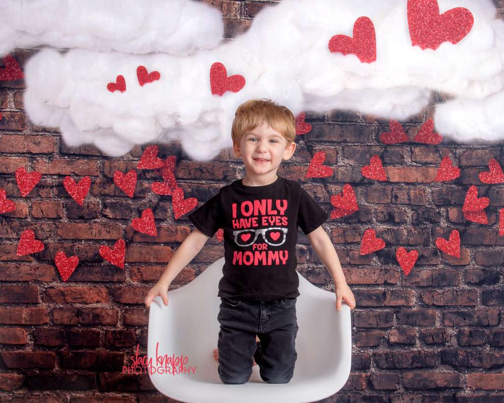 Preschool  boy photographed on Valentines Day backdrop with hearts and clouds during mini session