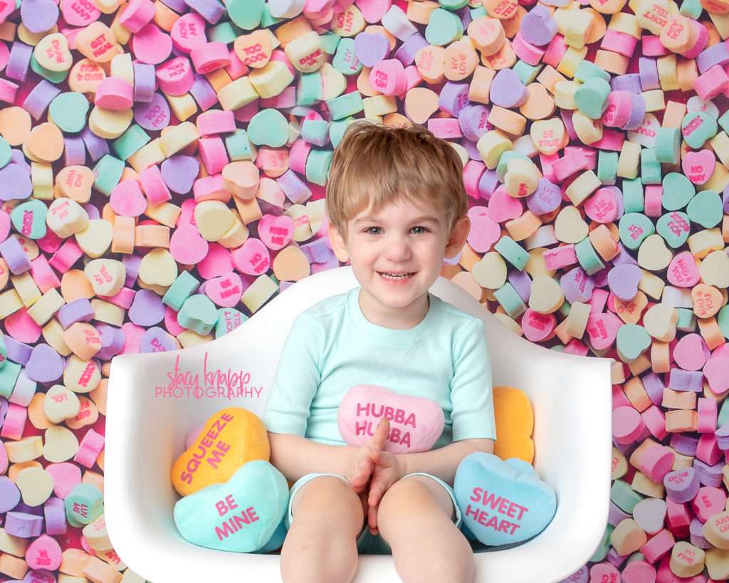 Preschool boy photographed on candy heart backdrop during mini session