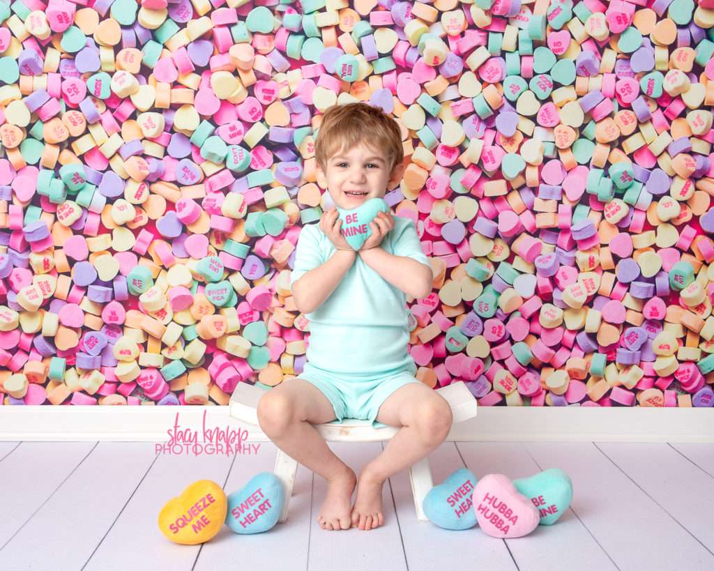 Preschool boy photographed on candy heart backdrop during mini session