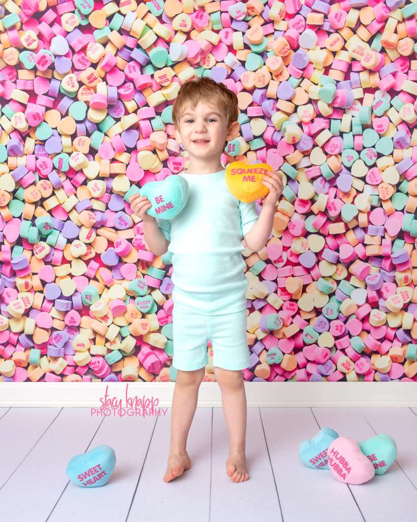 Preschool boy photographed on candy heart backdrop during mini session