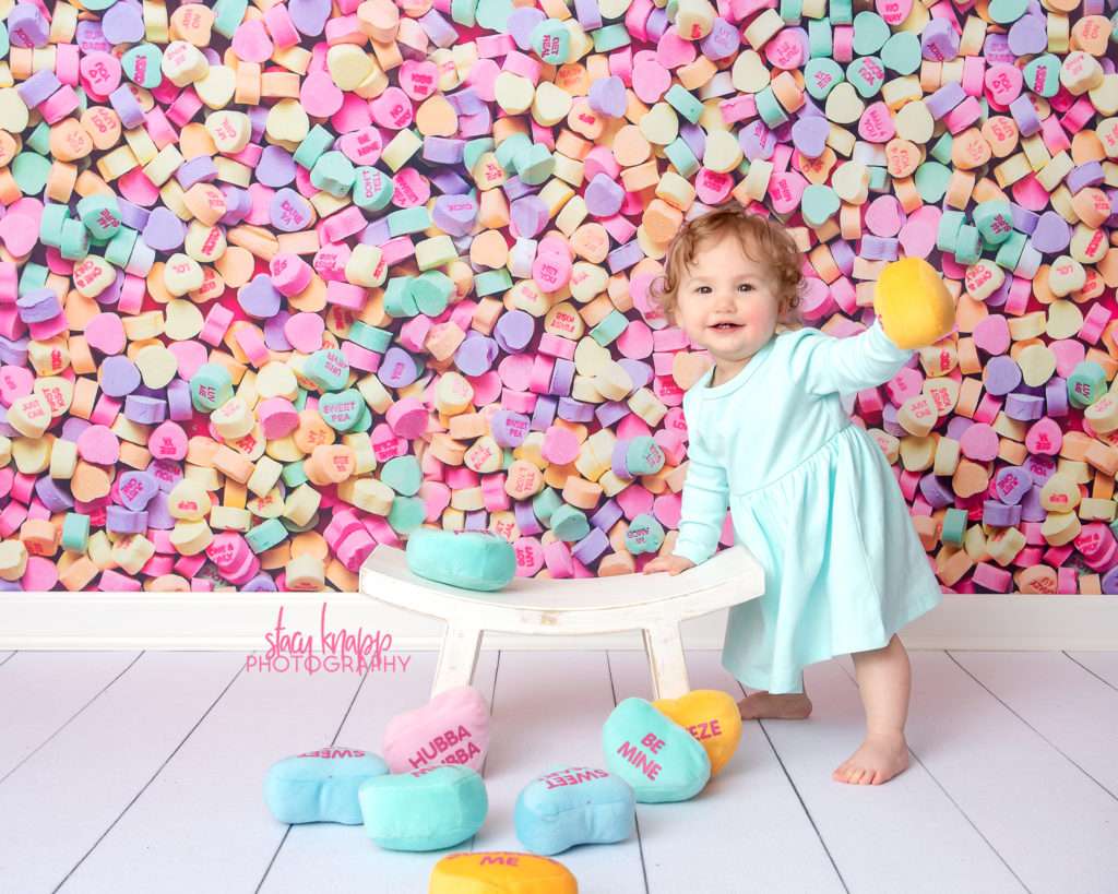 Baby girl photographed on candy heart backdrop during mini session