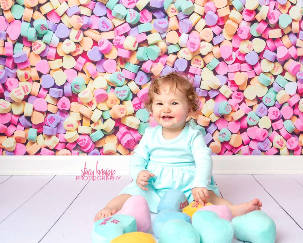 Baby girl photographed on candy heart backdrop during mini session