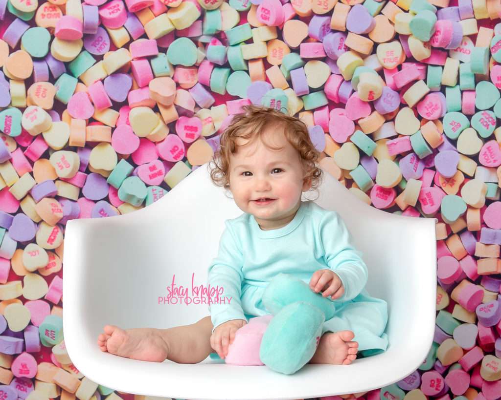 Baby girl photographed on candy heart backdrop during mini session
