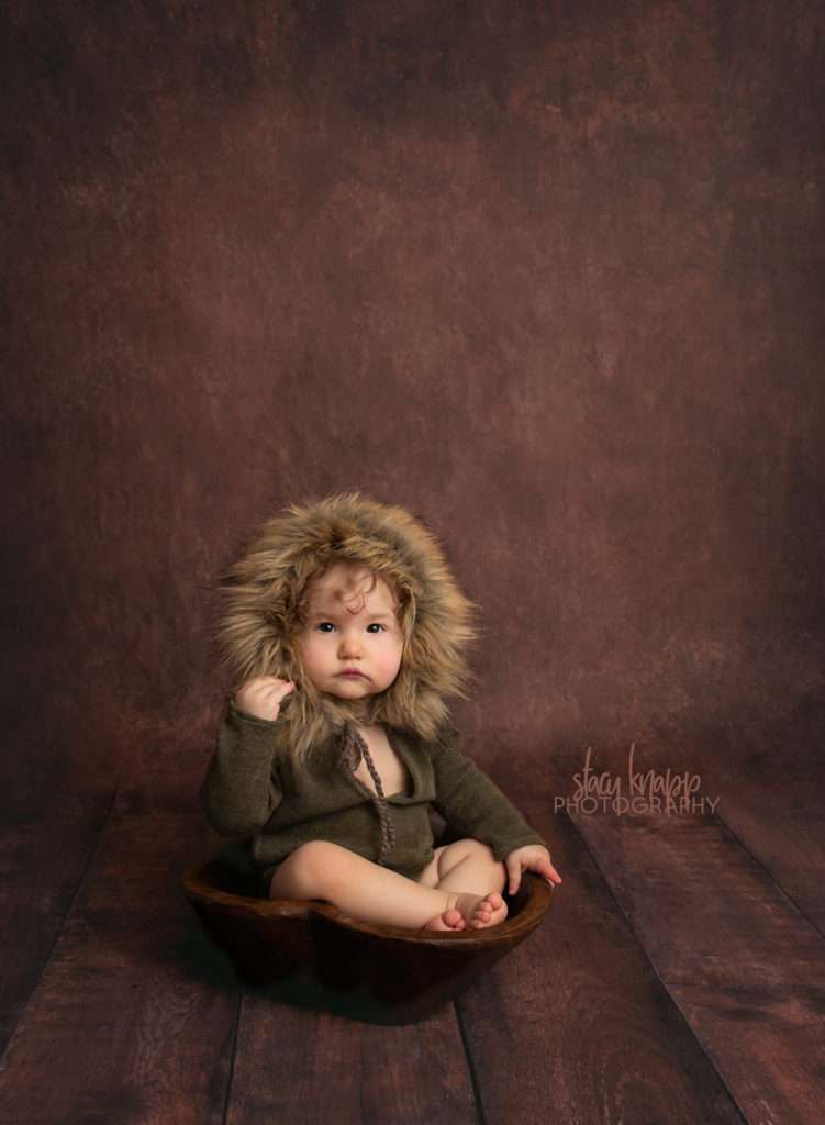 Photo of toddler girl in green fuzzy hood outfit on dark wood backdrop