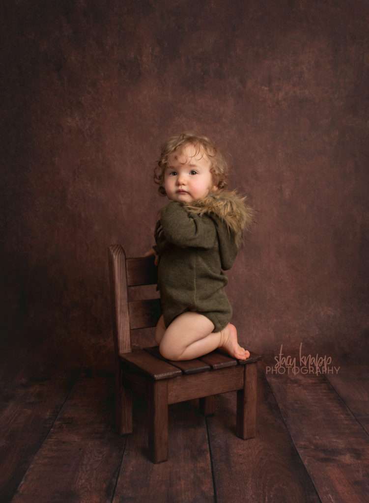 Photo of toddler girl in green fuzzy hood outfit on dark wood backdrop