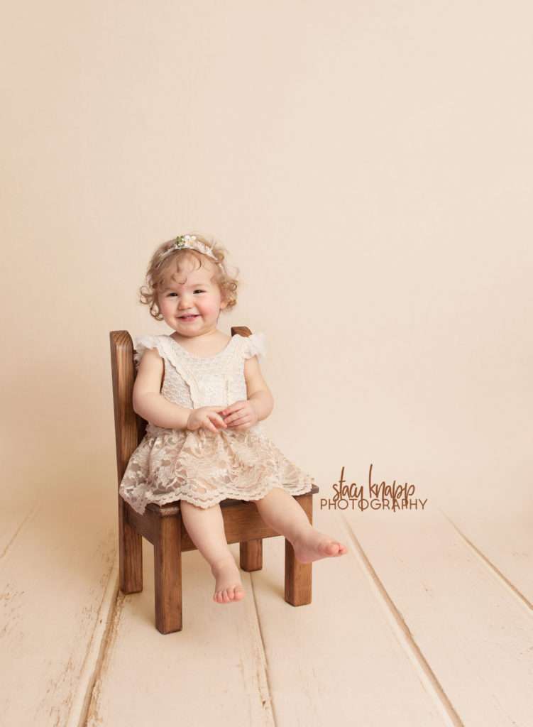 Photo of toddler girl in beige dress on beige wood backdrop in sitter chair