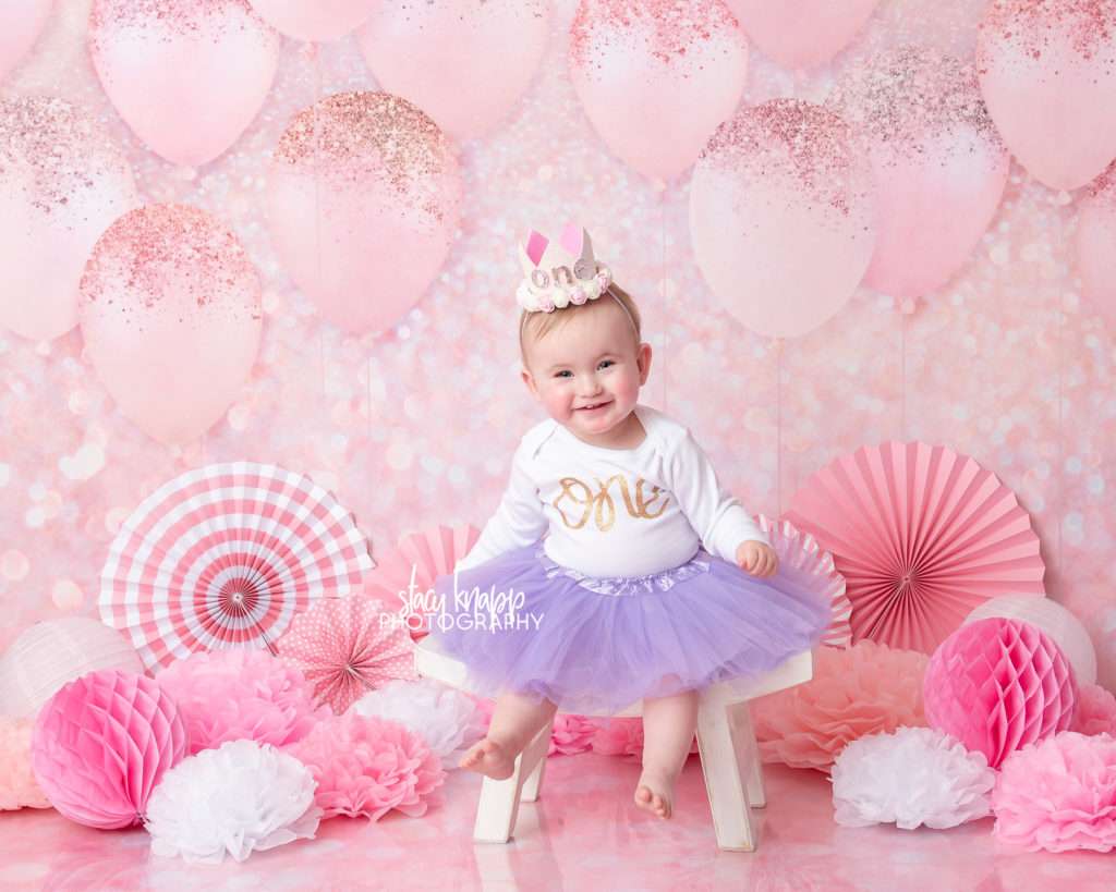 Photo of one-year-old girl birthday session with pink balloons and purple tutu