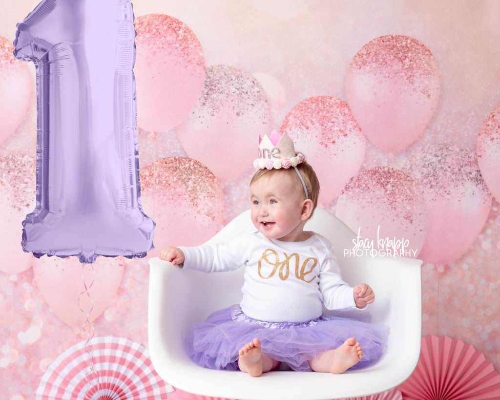 Photo of one-year-old girl birthday session with pink balloons and purple tutu