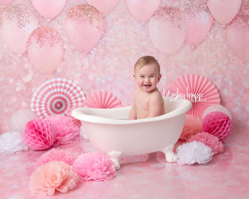 Photo of one-year-old girl birthday splash session with pink balloons in tub