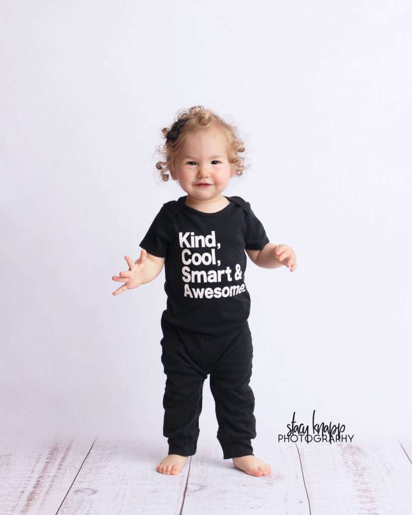 Toddler baby girl on white wood backdrop wearing kind cool smart and awesome outfit