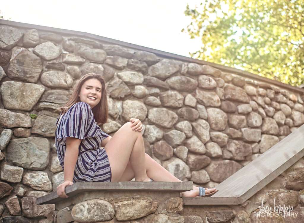 Senior girl sitting on rock wall in romper