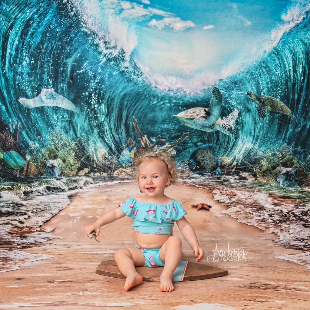 Baby girl in flamingo bathing suit in an ocean scene with a sea turtle