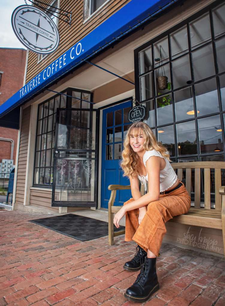 High school senior girl sitting outside on bench in front of coffee shop