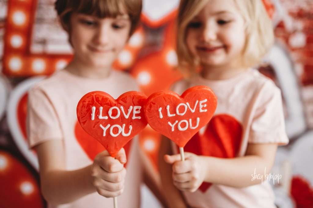Brother and sister celebrating valentines day at Stacy Knapp Photography holding heart lollipops
