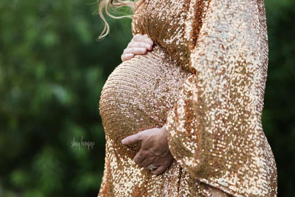 Close-up maternity photo of a pregnant mother in a gold glittery gown at the Viles Arboretum in Augusta, Maine by photographer Stacy Knapp Photography